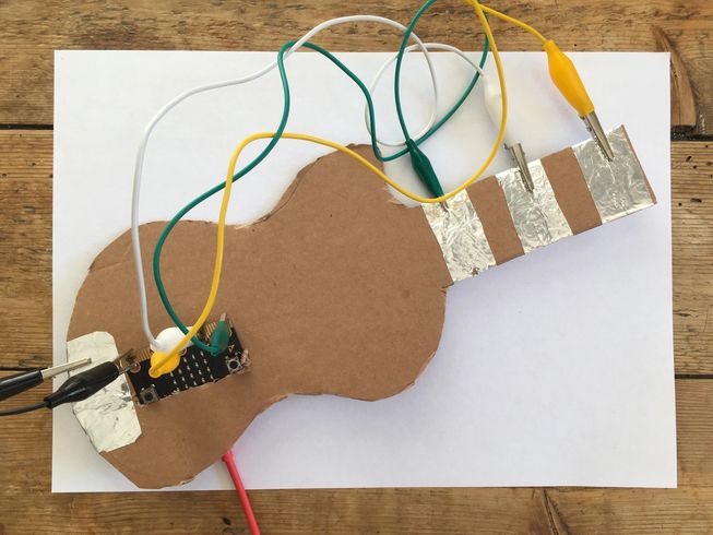 photo showing tin foil pads wired up to micro:bit pin 0, 1, 2 and GND on a cardboard guitar 
