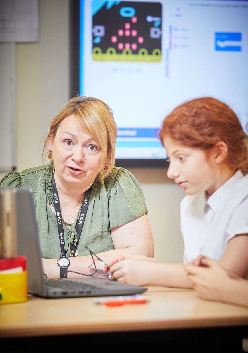 Female teacher sitting with a pupil explaining how the micro:bit works